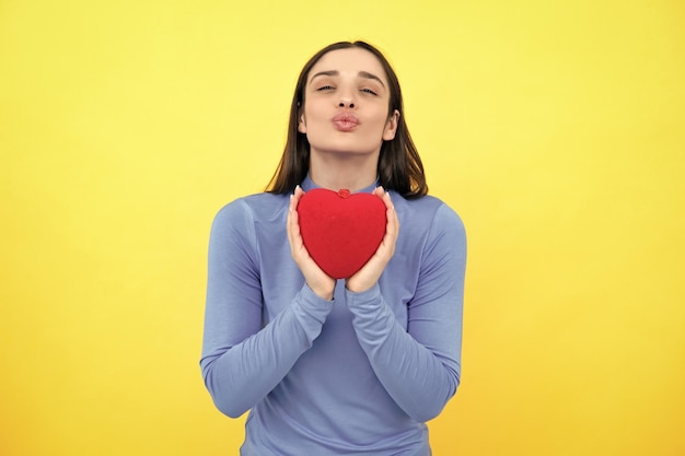 Meisje voelt liefde Gelukkige vrouw houdt rood hart Mooi vrouwelijk model poseren op geïsoleerde geel