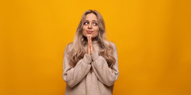 Meisje vouwde haar handen samen en smeekt op een oranje achtergrond