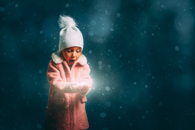 Foto meisje waait in de sneeuw op een zwarte achtergrond op kerstavond
