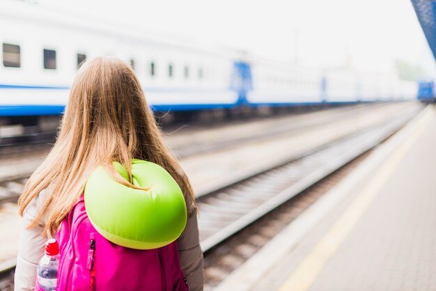 Meisje wacht op de trein. meisje met een rugzak en met groene nek kussen