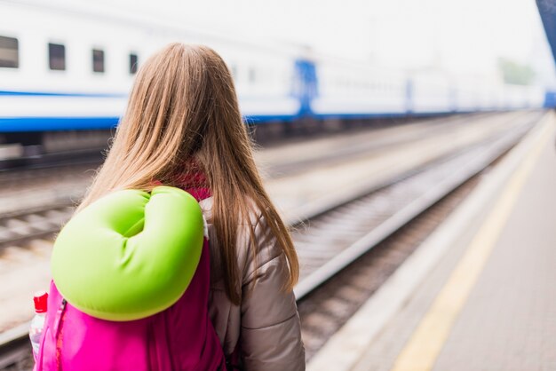 Meisje wacht op de trein. meisje met een rugzak en met groene nek kussen