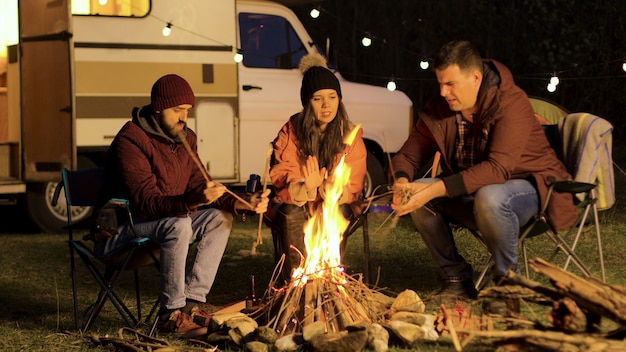 Meisje warmt haar handen op terwijl haar vriend het vuur sterker maakt. kamp vuur. retro camper. gloeilampen.