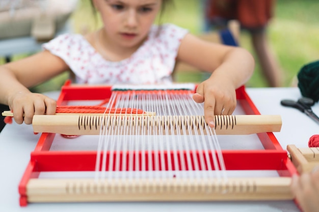 Meisje weeft klein tapijt met patroon tijdens masterclass weven meisje bestudeert hoe te weven op handmatig tafelgetouw proces van creatie handgemaakt concept