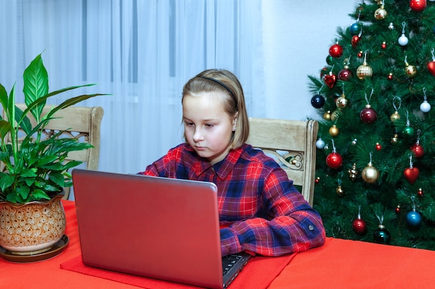 Meisje werkt achter laptop op de achtergrond van de kerstboom