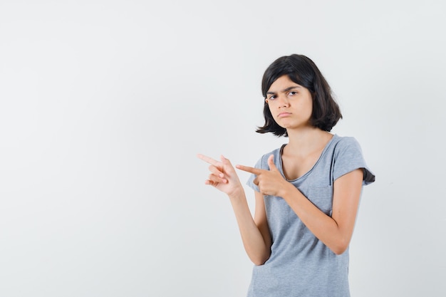 Meisje wijst naar de linkerkant in t-shirt en kijkt twijfelachtig. vooraanzicht.