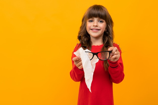 meisje wrijft bril met een servet op een oranje muur