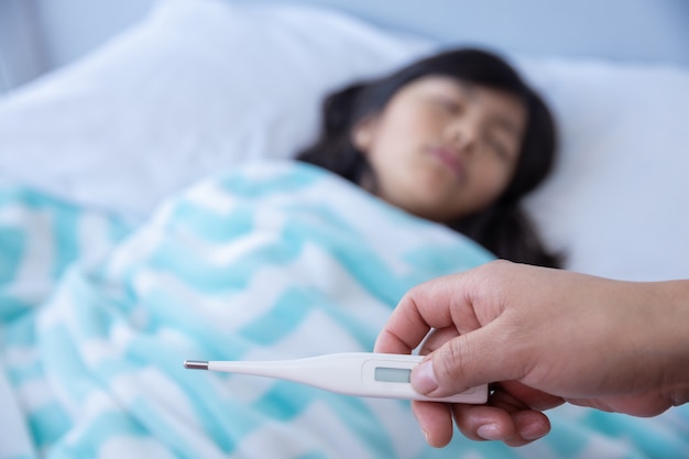 Meisje ziek in bed met coronavirus en de thermometer van de artsenholding