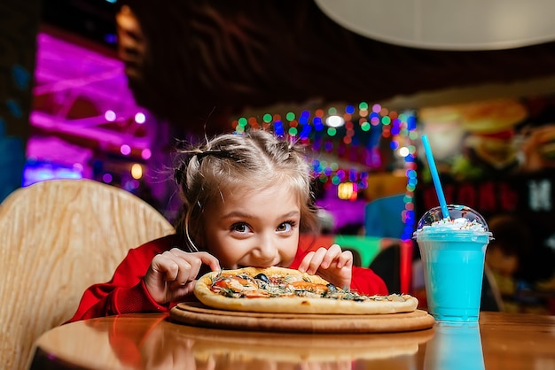 Meisje zit aan een tafel en eet pizza