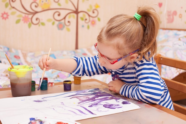 Meisje zit aan tafel en tekent verf op wit papier