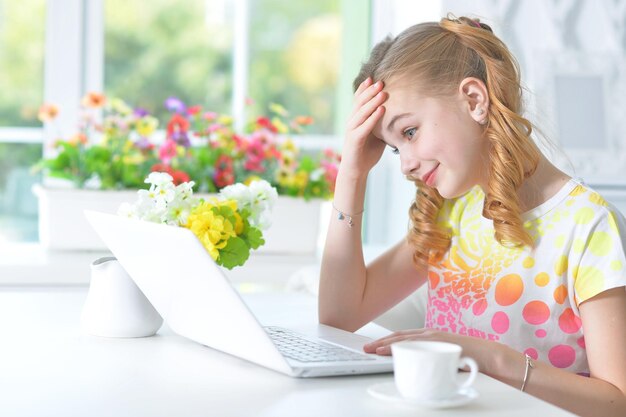 Meisje zit aan tafel met een laptop.