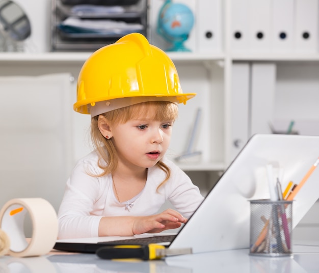 Meisje zit in de helm in de buurt van de laptop en spelen