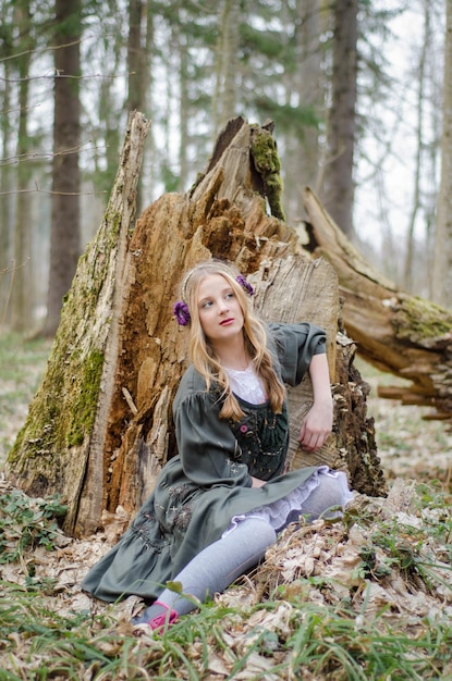 Meisje zit in het bos in de buurt van neergestorte boom