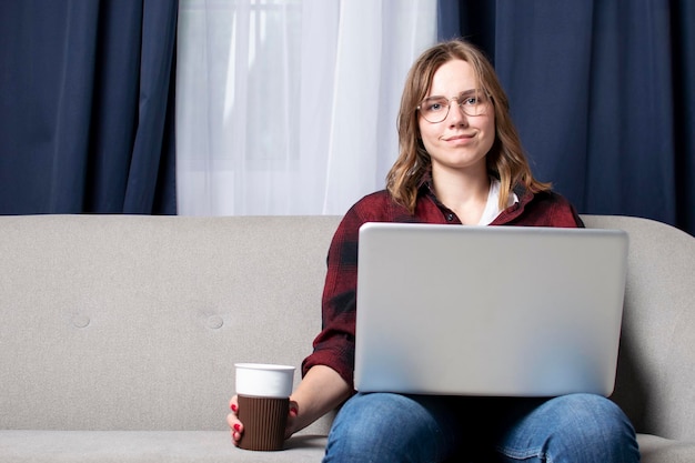 Meisje zit op de bank met een laptop en kijkt naar een video vrouwelijke freelancer werkt thuis
