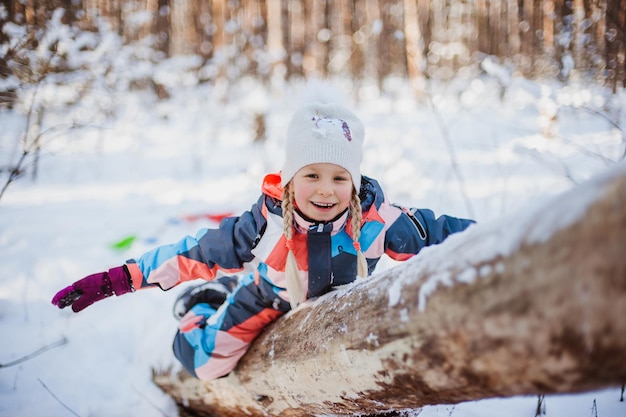 Meisje zit op de sneeuw in overall in het bos