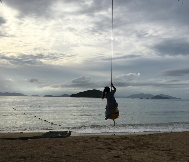 Foto meisje zit op een schommel op het strand tegen de lucht.