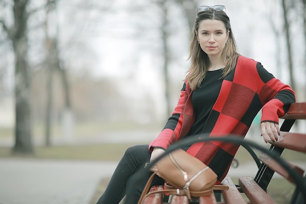 meisje zit op een tuinbank / mooi model poseren zittend in jas op bankje in stadspark, mooie meid