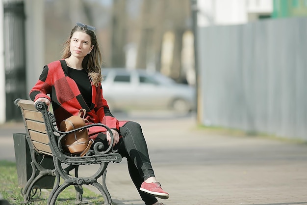 meisje zit op een tuinbank / mooi model poseren zittend in jas op bankje in stadspark, mooie meid