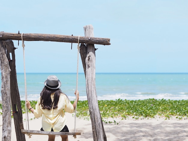 meisje, zittend in een houten schommel op het strand.