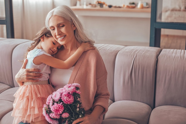 Meisje zittend op de schoot van de grootmoeder met boeket bloemen thuis