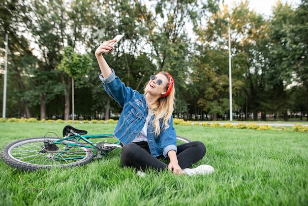 meisje, zittend op het gras en neemt selfie met de fiets op uw smartphone