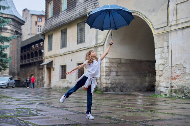 Meisjekind in de regen met een paraplu, achtergrond van de toeristen de oude stad