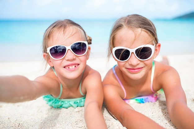 Meisjes die pret hebben bij het tropische strand spelen samen bij ondiep water. Aanbiddelijke kleine zusters bij strand tijdens de zomervakantie