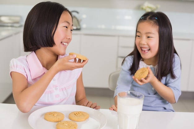 Meisjes die van koekjes en melk in keuken genieten