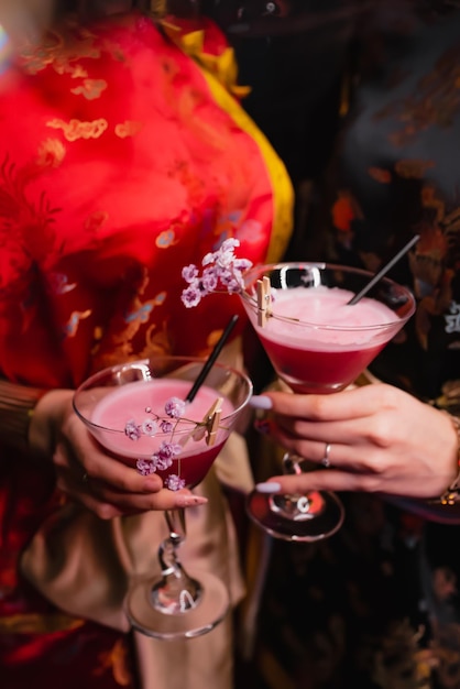 Meisjes in kimano houden twee rode cocktails vast die versierd zijn met roze bloemen. Feestconcept, nachtclub