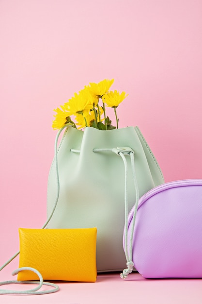 Meisjes leren accessoires in felle pastelkleuren: handtas, handtas, make-uptasje en bloemen over roze achtergrondkleur