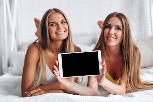 Meisjes liggen op het bed en tonen een tabletscherm