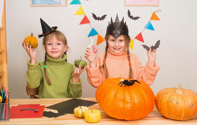 Foto meisjes maken halloween decoraties grappige zussen in halloween kostuums met pompoenen spinnen vleermuizen