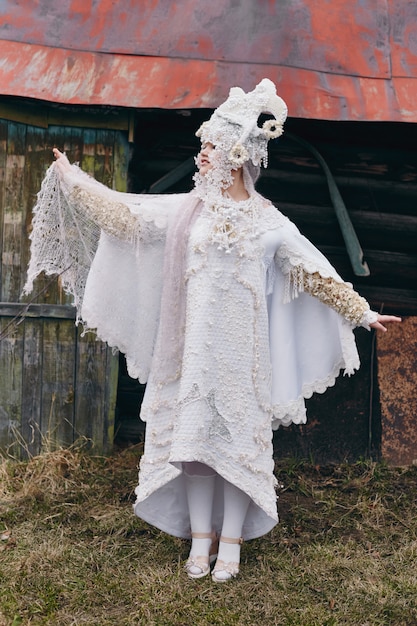 Meisjes nieuwe etnische Russische mode Vogue creatieve kleding poseren in de buurt van oud huis, witte jurk en hoed