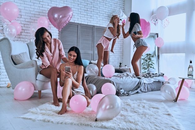 Meisjes plezier. Vier aantrekkelijke jonge vrouwen in pyjama die glimlachen terwijl ze een slaapfeestje houden in de slaapkamer met overal ballonnen