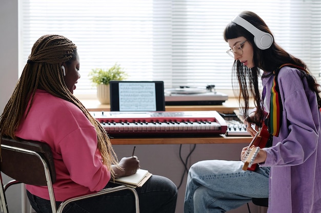 Meisjes schrijven samen een nieuw nummer met behulp van piano en gitaar tijdens de repetitie in de studio