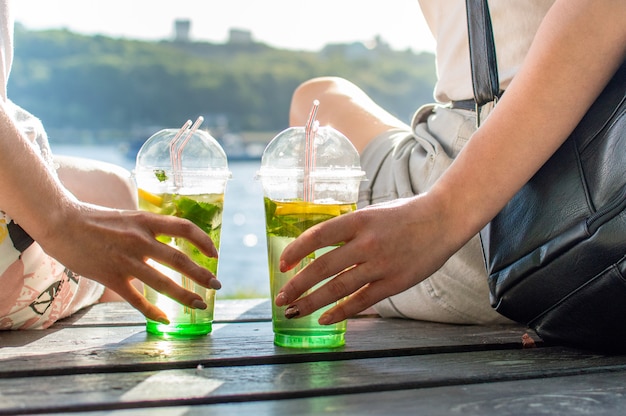 Meisjes zitten op een bankje en drinken mojito uit plastic glazen