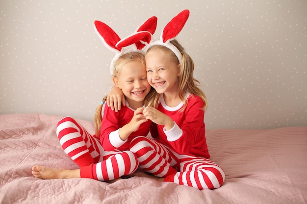 meisjes zussen blond zit thuis op het bed in rode pyjama's en konijnenoren