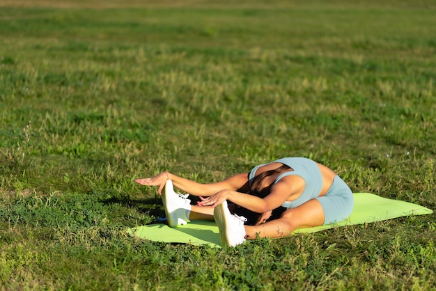 Meisjesatleet die zich uitstrekt in het zomerpark van de stad Het concept van geweldige fitness