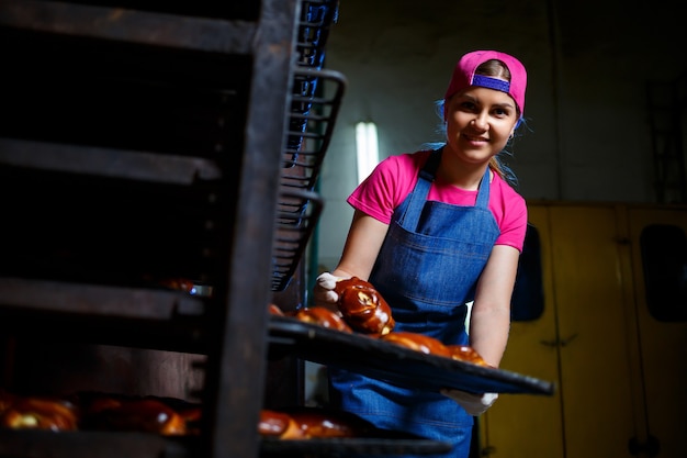 Meisjesbakker houdt een dienblad met warme gebakjes in de bakkerij. Productie van bakkerijproducten. Vers krokant gebaksrek