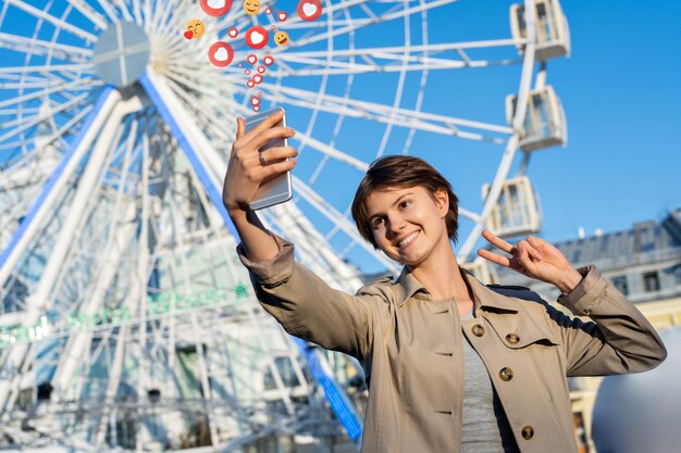 Meisjesblogger die telefoon gebruikt, maakt selfie voor sociale media met emoji in de stad