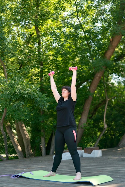 Meisjescoach voert oefeningen uit met halters in het park. Buiten fitnessen. Handtraining met halters. Oefeningen voor beginners.