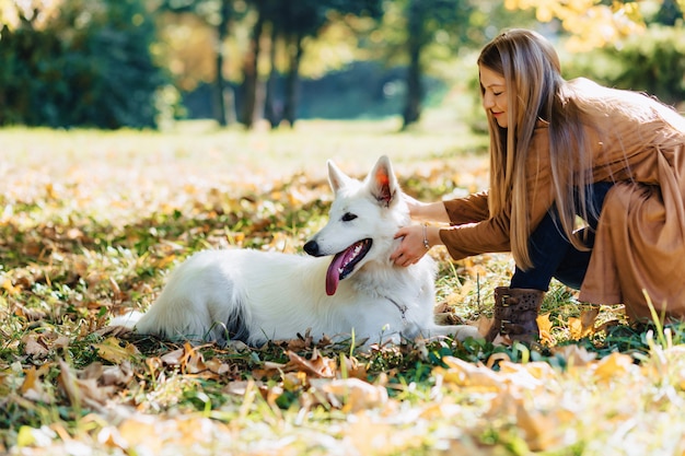 Meisjesgangen bij de herfstpark met jonge witte Zwitserse herdershond