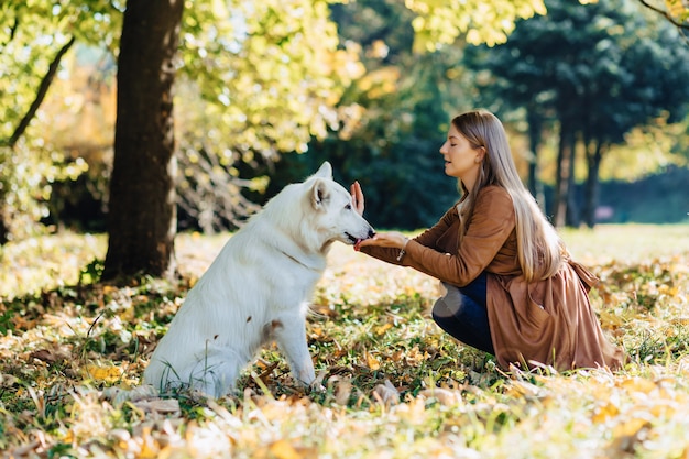 Meisjesgangen bij de herfstpark met jonge witte Zwitserse herdershond