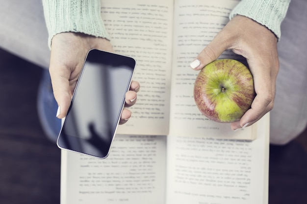 Meisjeshanden die smartphoneappel en open boeken houden