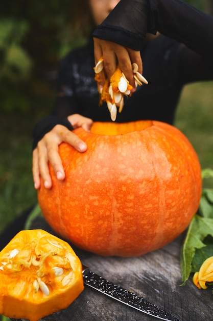 Meisjeshanden die zaden en vezelmateriaal van pompoen trekken alvorens voor Halloween te snijden