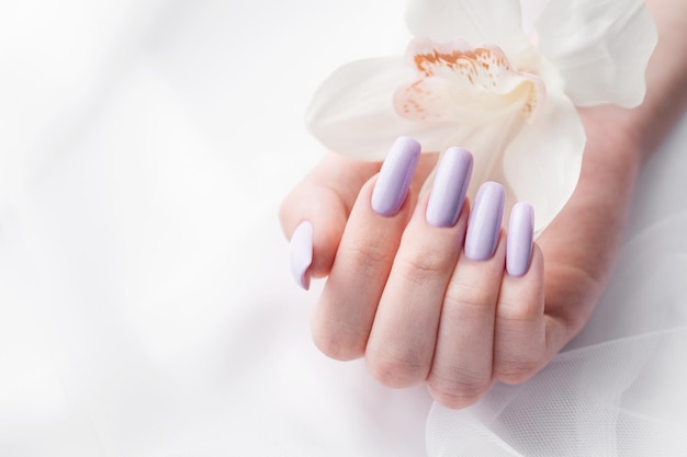 Meisjeshanden met delicate paarse manicure en orchideebloemen