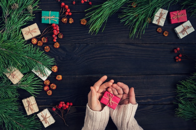 Meisjeshanden met kerstcadeau op de achtergrond van donkere planken van pijnboomtakken