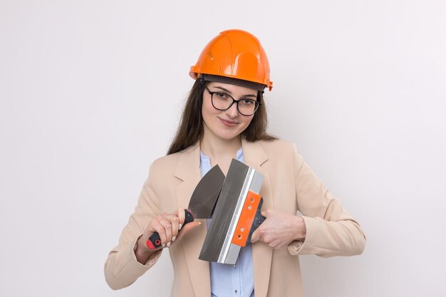 Meisjesingenieur in een oranje bouwhelm met pleistergereedschap in haar handen op een witte achtergrond