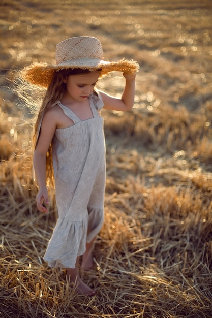 Meisjeskind met lang haar dat over het veld loopt dat een hoed met lang haar draagt tijdens zonsondergang