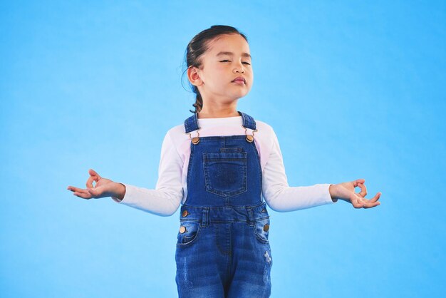 Meisjeskind zen en meditatie in studio met ogen gesloten vrede en welzijn door blauwe achtergrond F