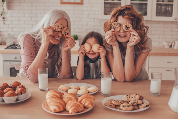 Meisjesmoeder en grootmoeder die ogen bedekken met koekjes die samen aan de keukentafel zitten